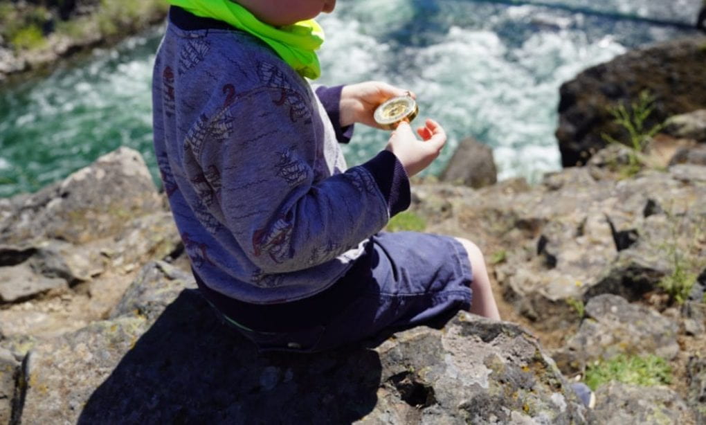 Little kid on rocks near river holding bronze compass