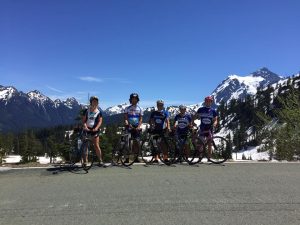 5 team members pose atop a road with snow capped mountains in the background
