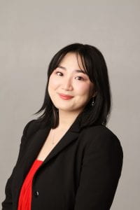 Asian gril wearing a black blazer and a red blouse smiling.