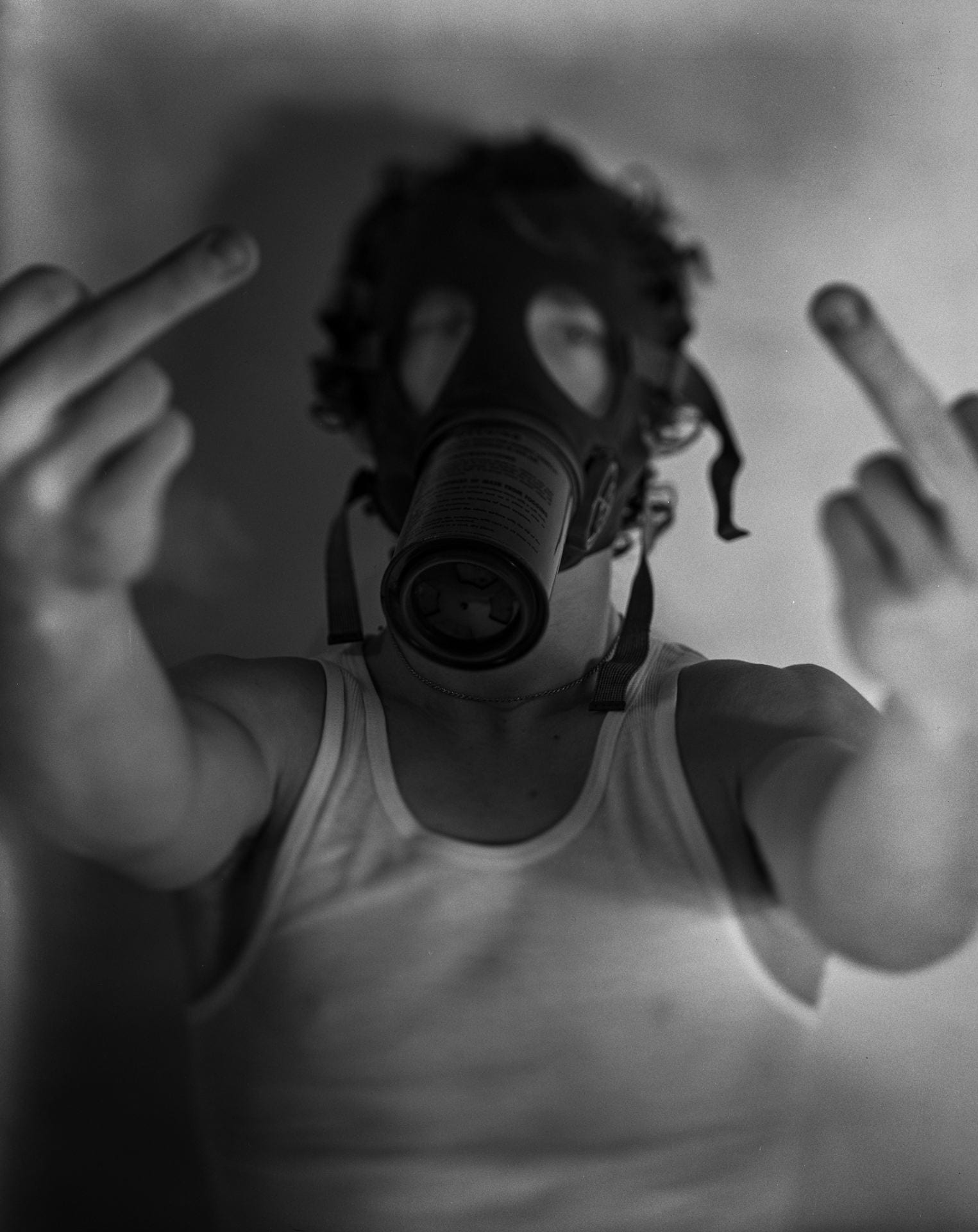A person in a gas mask holds two middle fingers up to the viewer