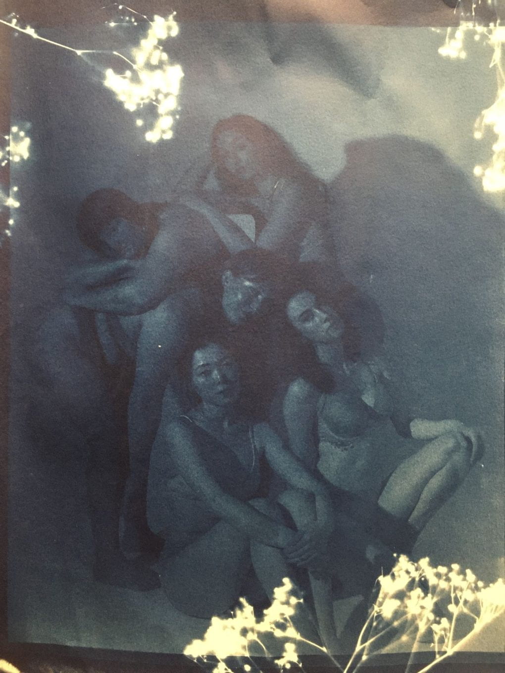 In dark blue cyanotype, women pose atop one another all looking at the viewer