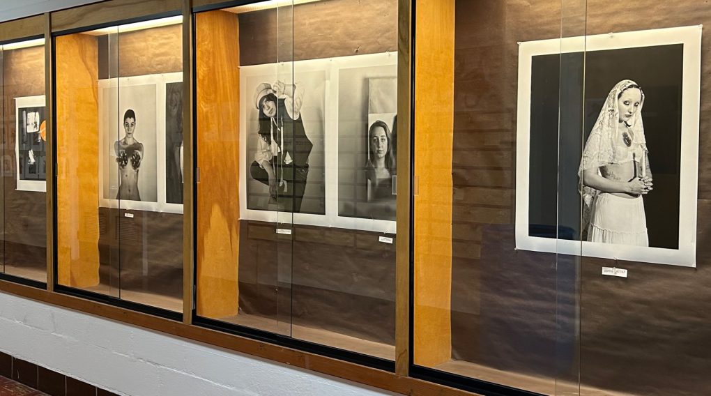 An image of large photographs behind glass cases. Five self portraits and a poster for the show.