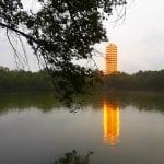 Tall building glowing orange with a lake in front of it.