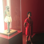 A student imitates the pose of a dancer statue in a display case