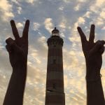 A student makes "peace signs" next to a red and white lighthouse