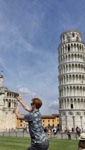 Student poses by the Leaning Tower of Pisa, appearing to hold up a neighboring building