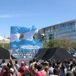 BMX riders do tricks, while an Argentinean flag waves in the foreground
