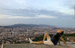 A student lays on a stone wall overlooking a coastal city