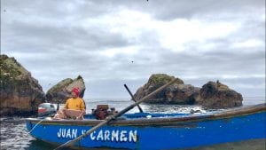 A man in a blue fishing boat displays his catch, with rocky isles behind him