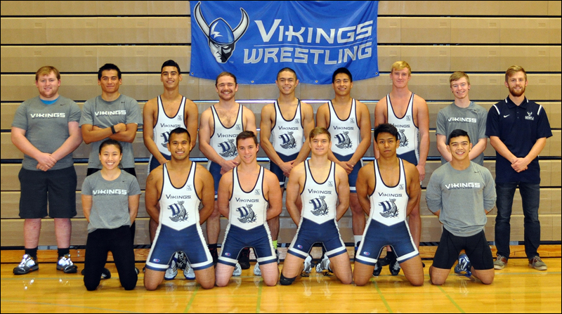 2016-17 WWU Wrestling Team poses in front of team banner attached to the bleachers in Carver gym